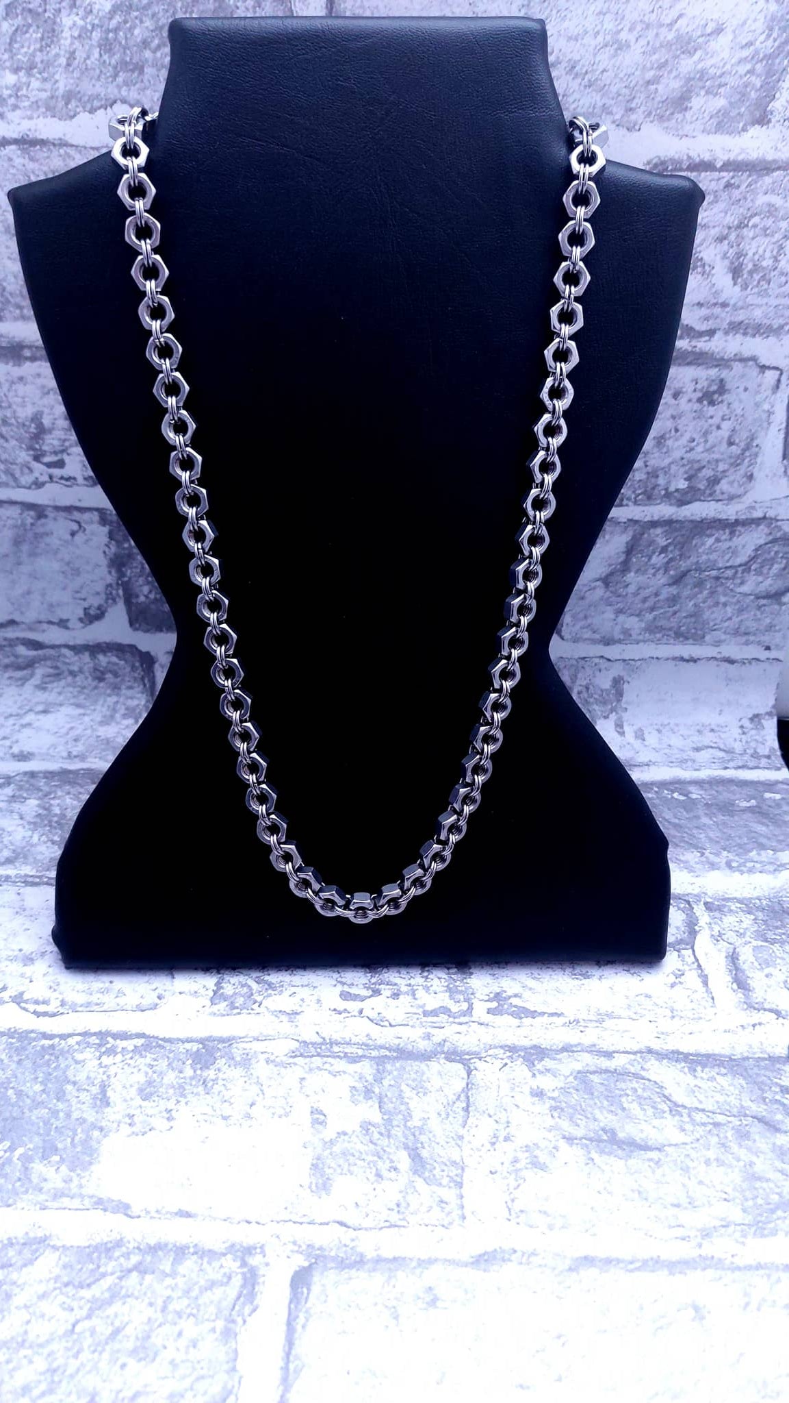 Silver chain necklace displayed on black necklace stand with brick wall background