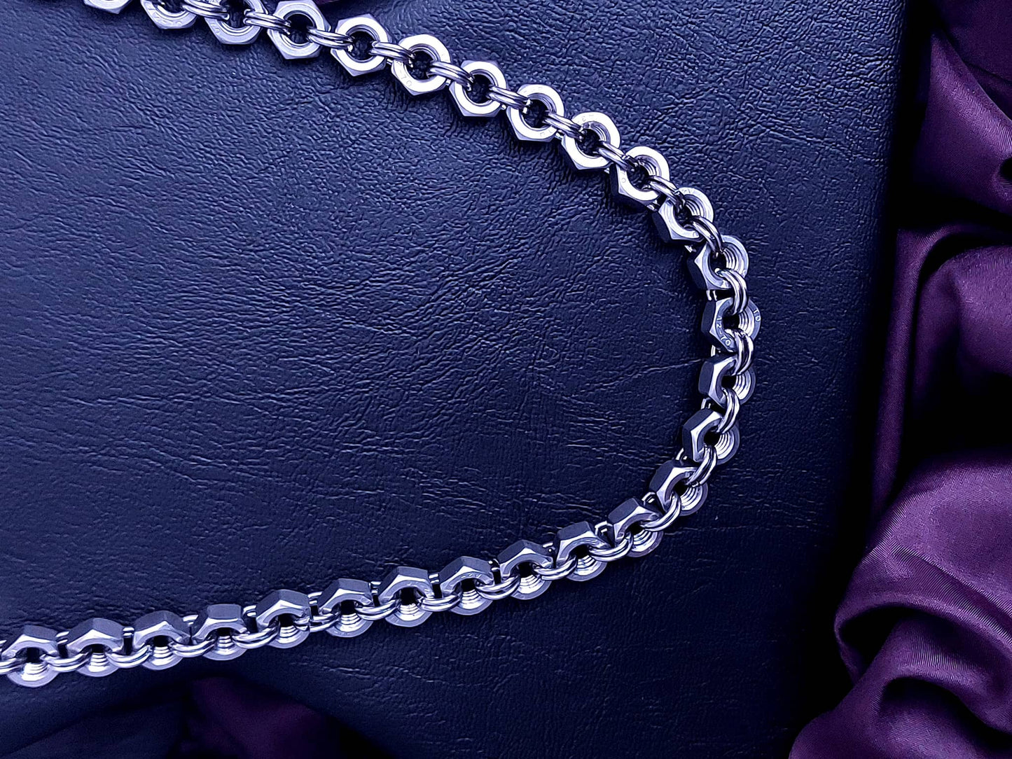 Silver chain necklace with thick links displayed on black leather background with purple fabric