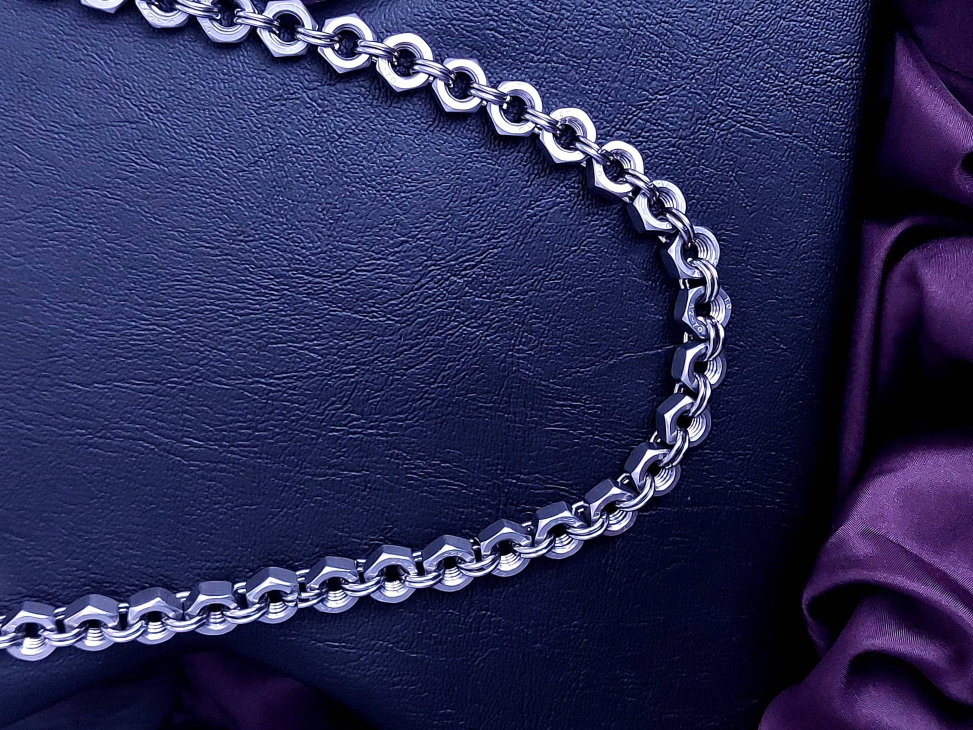 Silver chain necklace with thick links displayed on black leather background with purple fabric