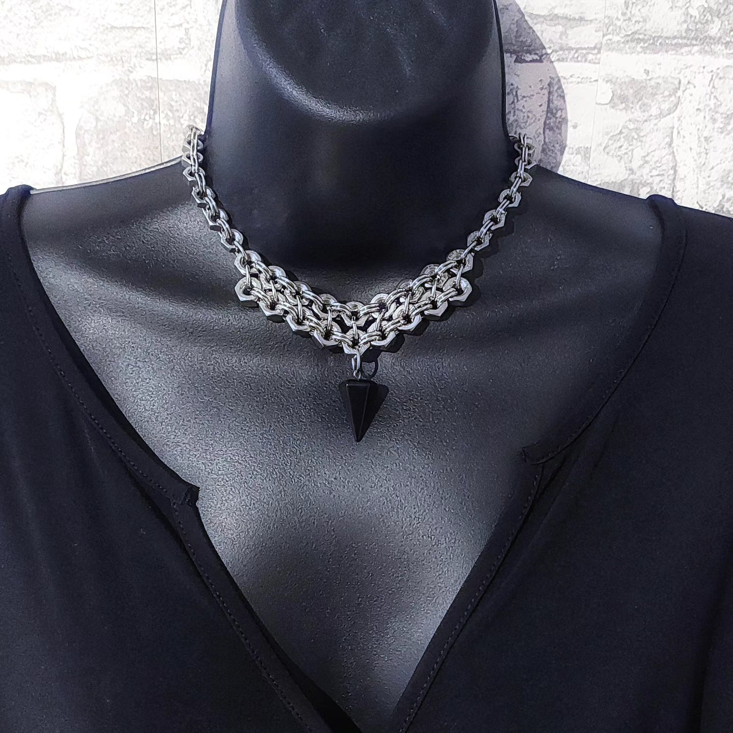 Silver chain necklace statement with black triangular pendant on mannequin wearing black top